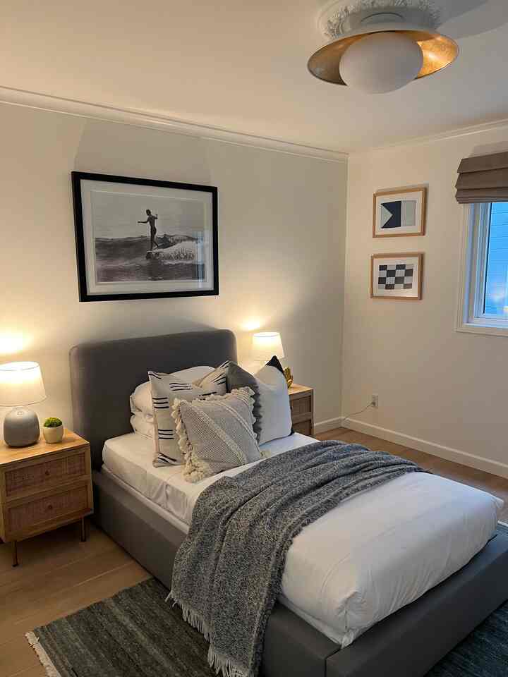 Natural-toned bedroom with gray bed frame and white bedding, featuring ocean-inspired wall art and a minimalist design