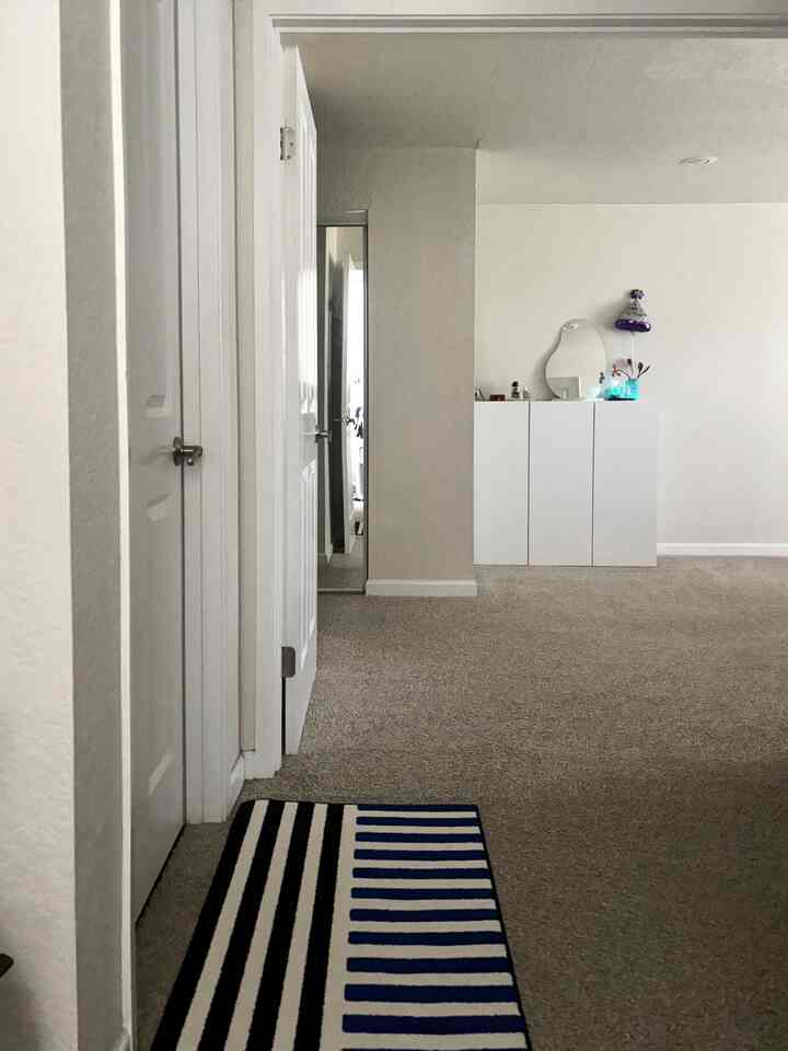 A simple space featuring white and beige tones in hallway and closet, with a blue striped rug as a color accent