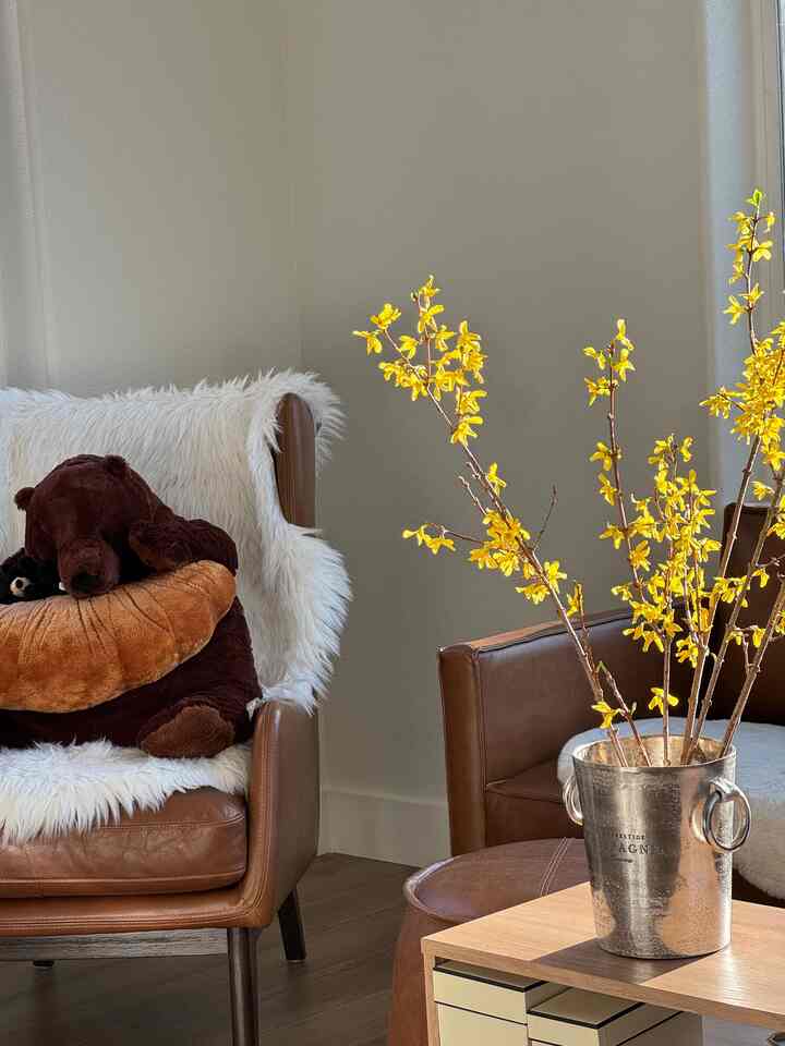 Bright and cozy living room with yellow flowering branches and brown leather armchairs