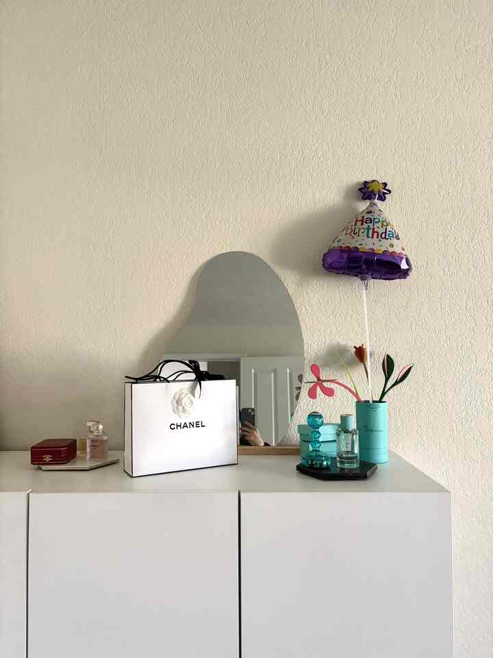 White-toned walk-in closet featuring a white shelf with decorative items and a uniquely curved mirror above
