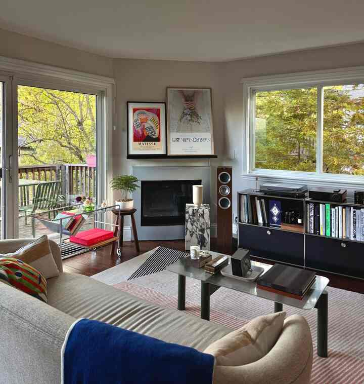 Bright light brown toned living room featuring a beige sofa, coffee table, bookshelf, and lush green forest visible through windows in a natural modern setting