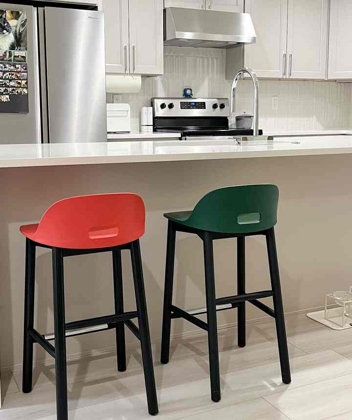 White-toned kitchen space featuring red and green stools, arranged for a minimal and modern cozy corner