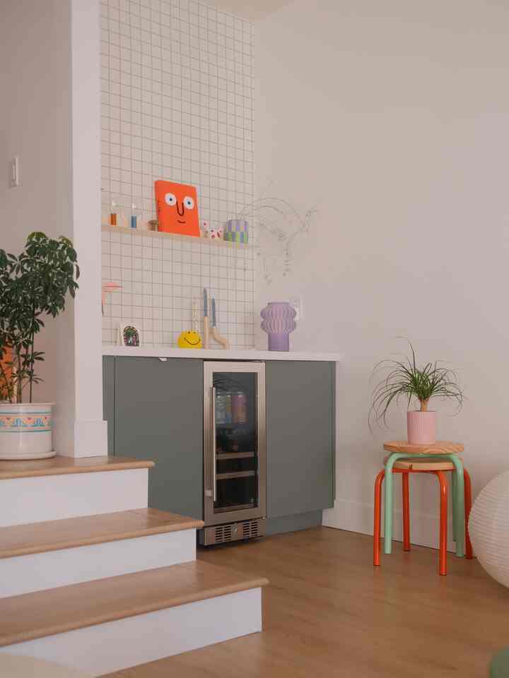 Natural wood tone and white colored home bar corner featuring a colorful stool and plants for cozy atmosphere