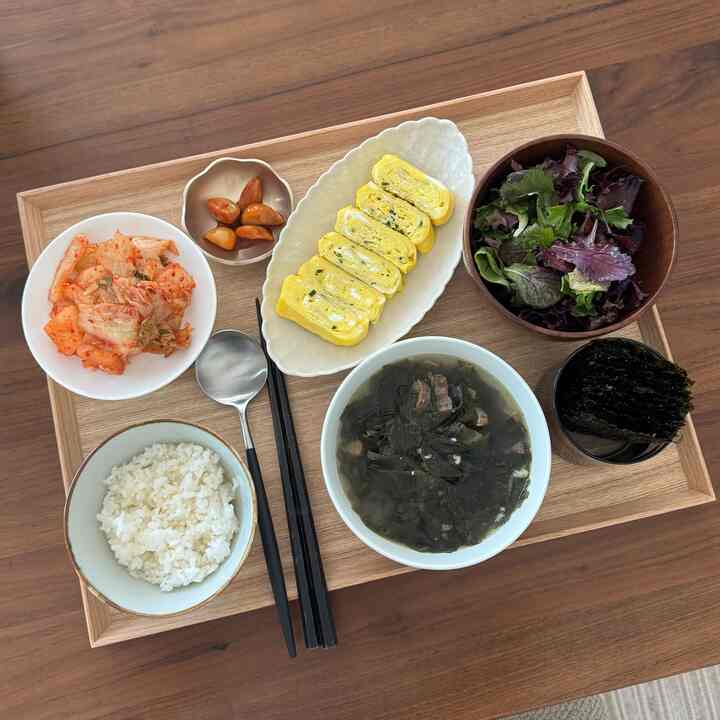 Natural-toned dining table with neatly arranged traditional Korean dishes and bowls, creating a clean meal setting