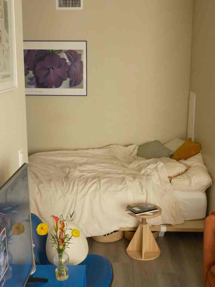 Natural-toned compact bedroom featuring white bedding and wooden stool with cozy atmosphere