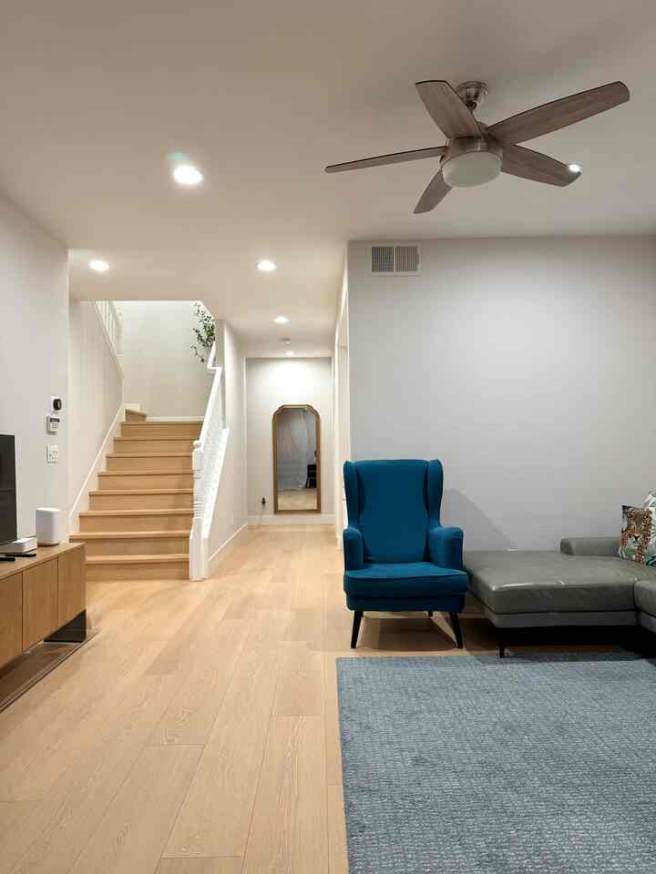Bright and clean living room with wood tone flooring and blue armchair, featuring ceiling fan and mirror arranged in space