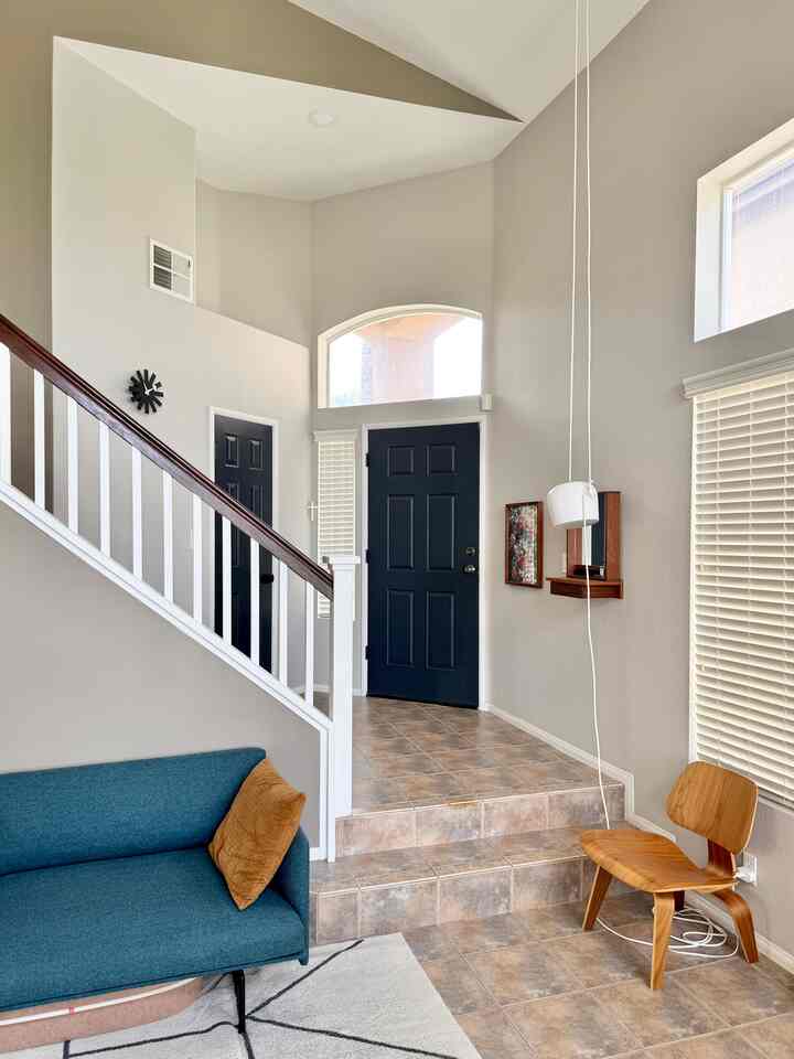 Natural toned entrance featuring wood tone chair and black doors, styled with mid-century modern elements in a clean interior