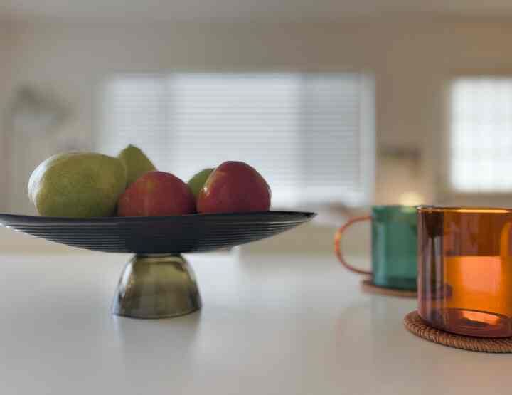 Bright-toned kitchen table featuring a decorative bowl with fruit and colorful mugs, creating a cozy home cafe vibe