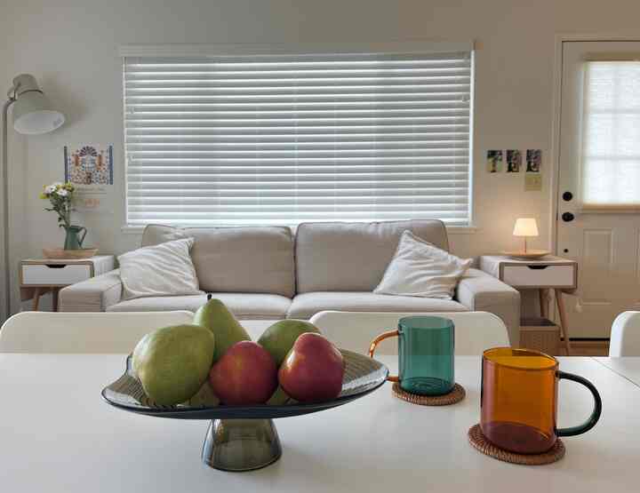 White and natural toned living and dining room with beige sofa and transparent mugs arranged in a cozy space