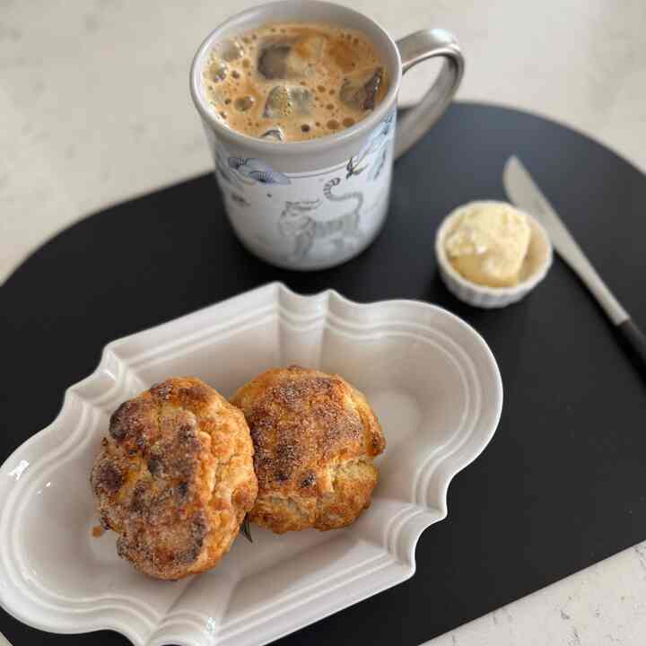 White and black toned home cafe setting featuring baked biscuits with clotted cream on a plate and iced americano in a patterned mug, cozy atmosphere