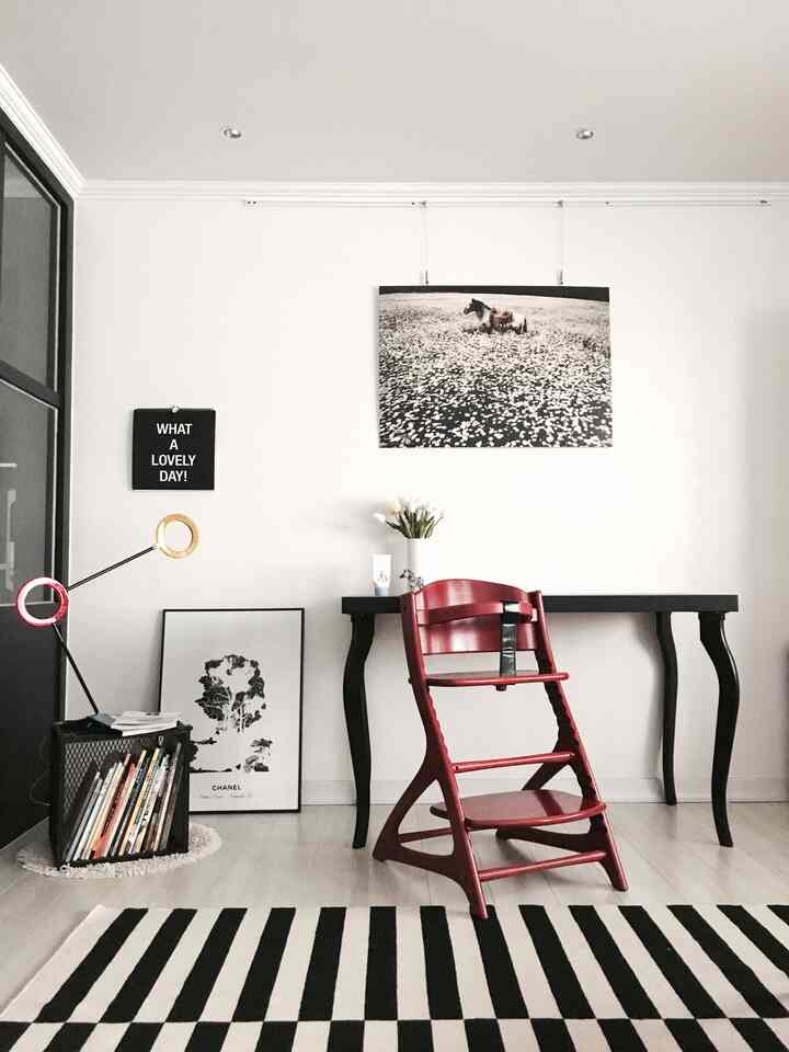 Natural kids' room with white and black striped rug featuring a central red baby chair and black desk against white walls