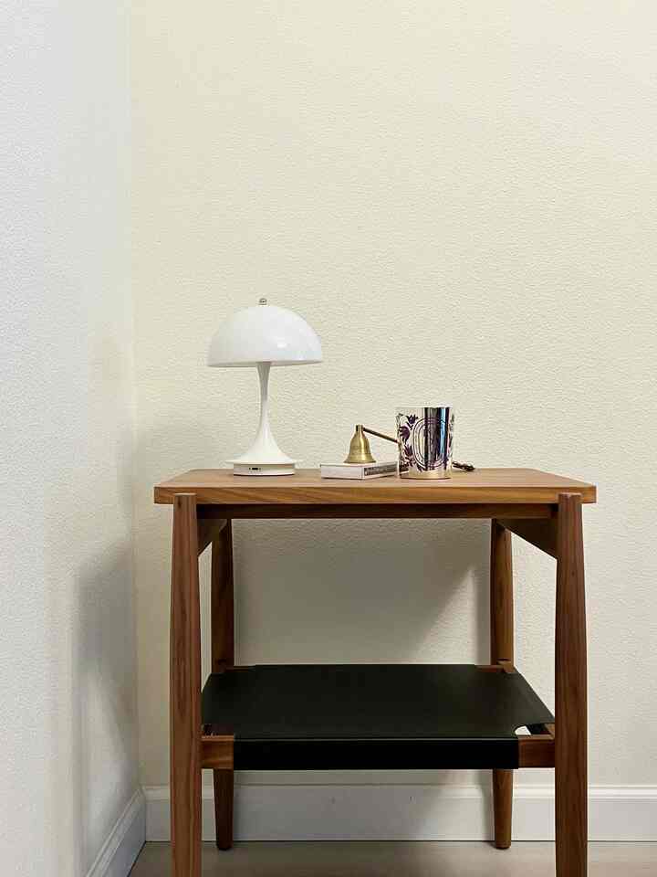 Ivory wall background with wood-tone side table featuring white table lamp, candle, and objets in a minimal setting