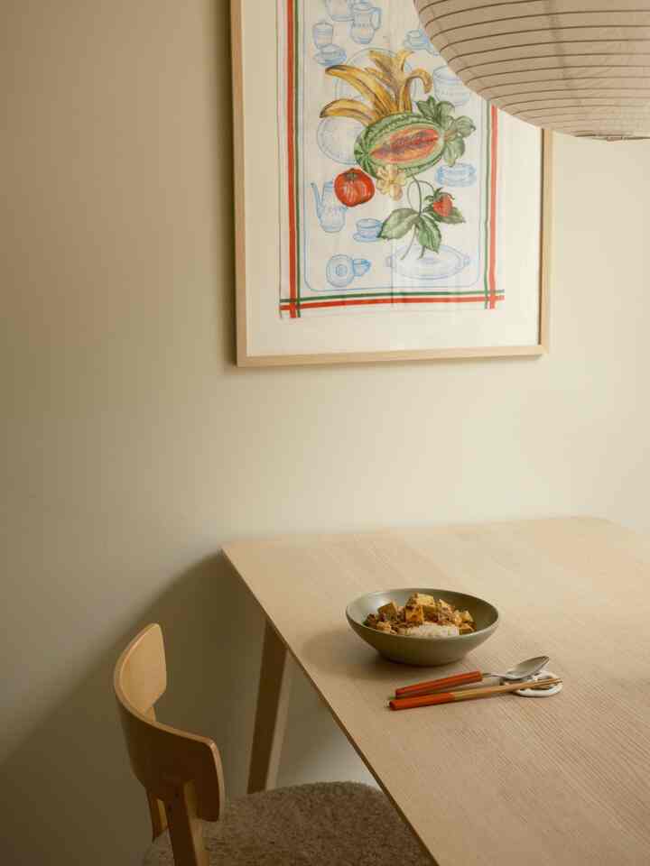 Beige wall and wood tone dining table with vintage tablecloth framed on wall in a simple two-person dining room