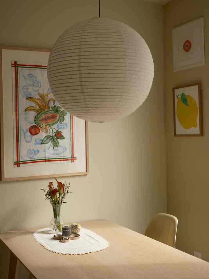 Beige-toned walls and natural wood-tone dining table featuring a vintage tablecloth and pendant light in a warm dining room
