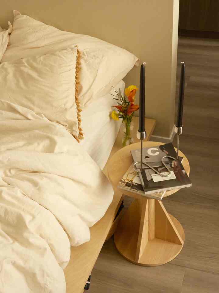 Ivory and brown toned bedroom featuring a wooden bed frame and stool with candles creating a cozy atmosphere.
