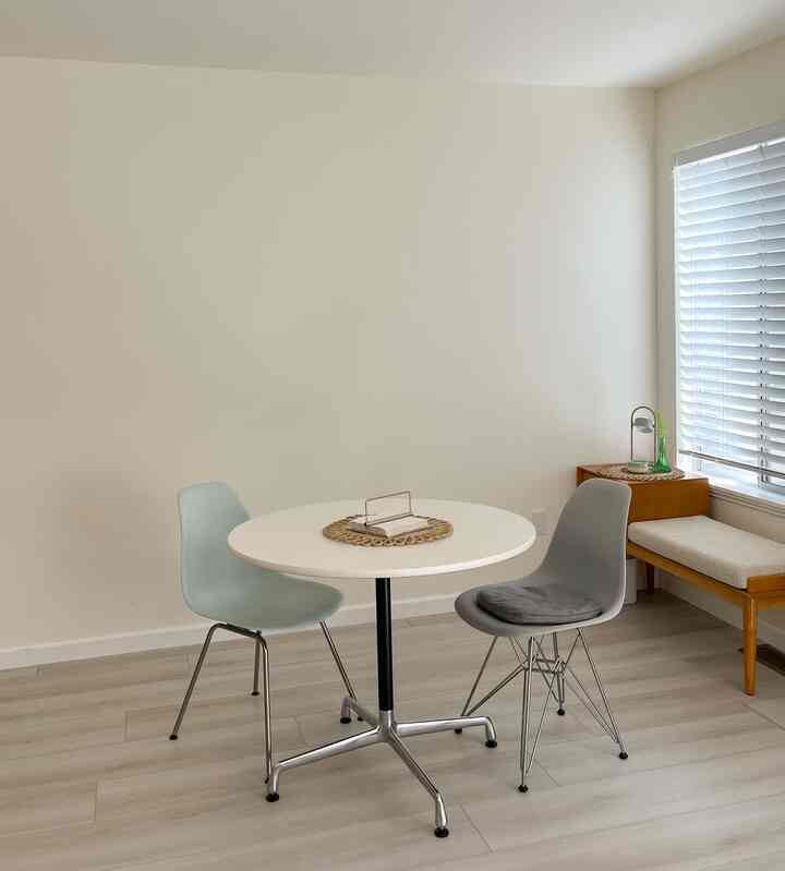 Natural wood tone and white dining room featuring a round dining table with two simple dining chairs