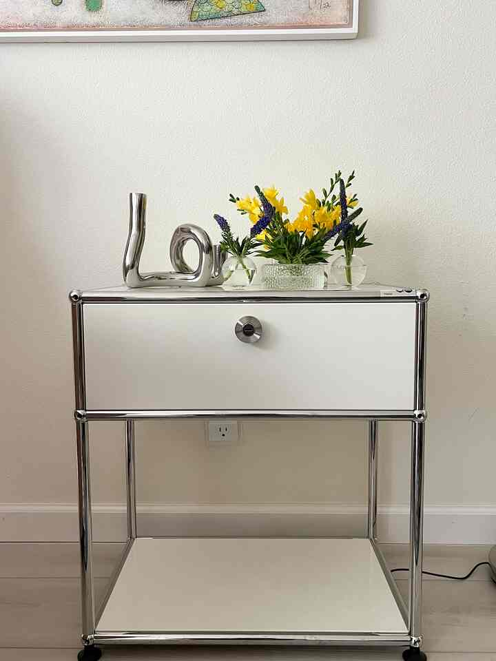 White and silver toned small storage cabinet featuring vases and decorative objects in a simple and modern space