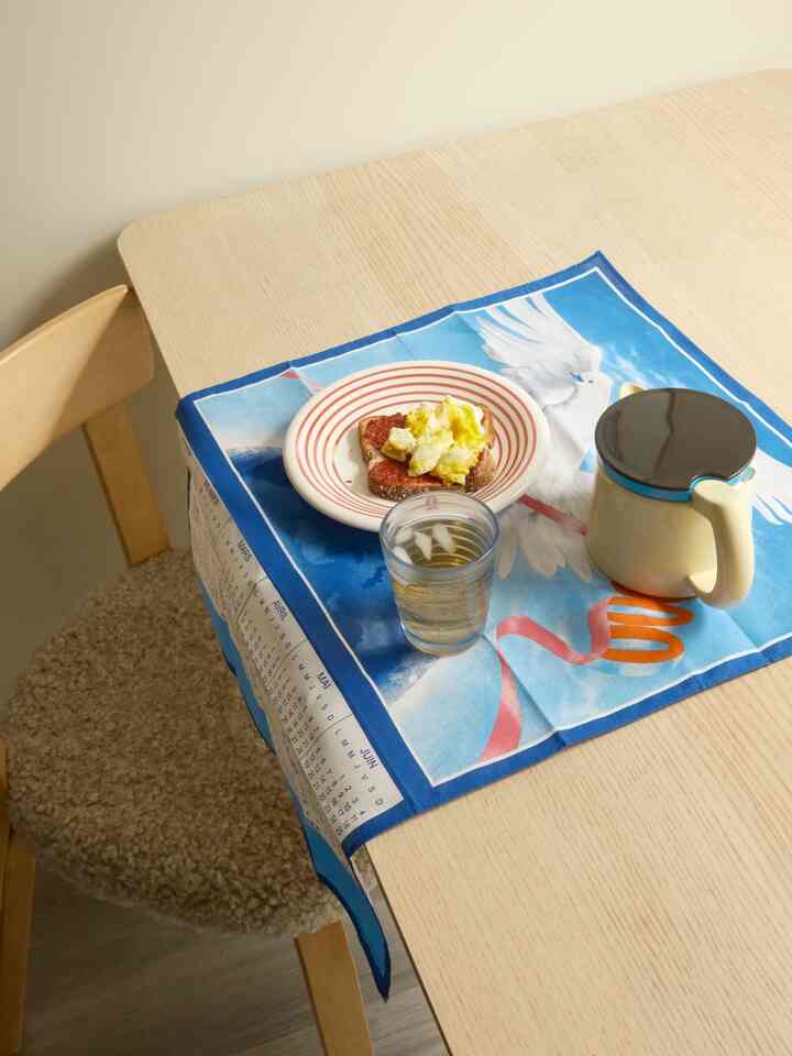 Natural-toned dining room featuring light wood dining table and chair with blue tablecloth and breakfast setup