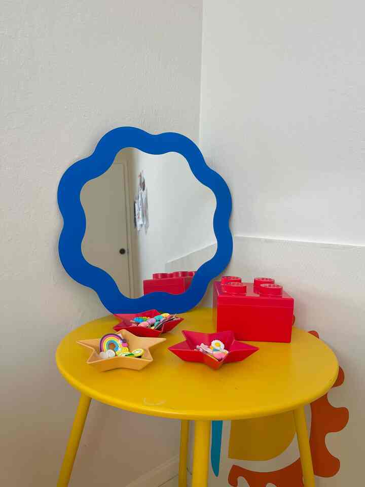 A yellow round table with a blue wavy mirror and star-shaped trays holding children's hair accessories, creating a kids' vanity space