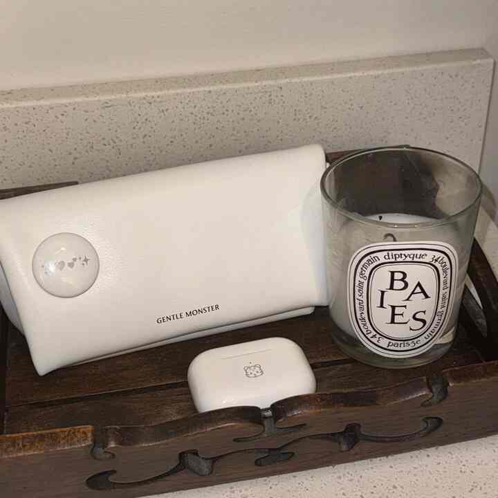 An entryway wooden basket in dark brown holding white AirPods case, glasses case, and a candle on a white countertop with coordinating tones