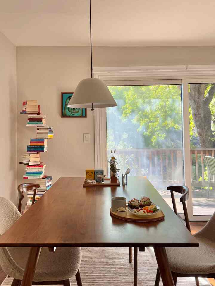 Wood-toned dining room with natural light, featuring a large wooden dining table, chairs, and a pendant light in a minimalist setting