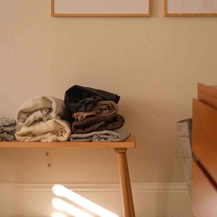 Warm wood tone and beige-walled bedroom dressing space featuring a wooden bench with folded clothes and simple furniture